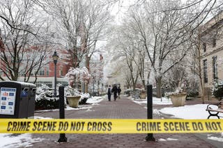Students walk across Brown University as police tape can be seen marking off areas where investigators are searching for evidence